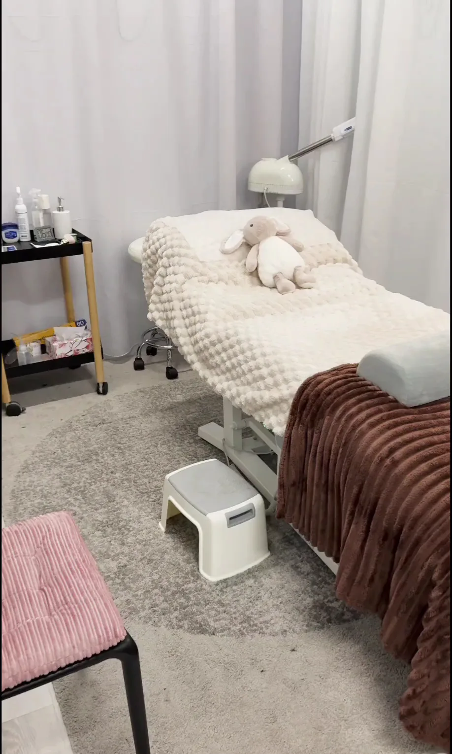 The empty treatment room — beauty bed, cream waffle throw, soft lighting